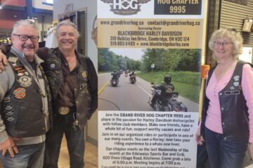 Photo taken during the Blackbridge Harley-Davidson dealership's International Women's Day Event "Inspire Inclusion" of three attendees standing next to a poster for the Grand Rive Hog Chapter 9995.