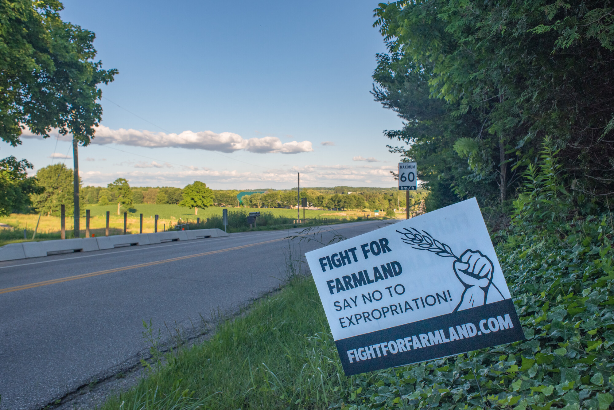 Photograph of a sign reading "FIGHT FOR FARMLAND, SAY NO TO EXPROPRIATION! FIGHTFORFARMLAND.COM" erected on a country road near the Waterloo Region.