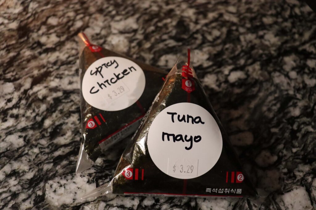Photo taken inside Taste of Seoul of two pre-wrapped onigiri sitting on a table with a different flavour written on each: one says "spicy chicken" and the other says "tuna mayo".