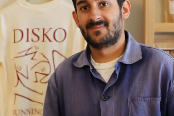 Photo of Arman Duggal, owner of Disko Coffee, posing inside his cafe in front of a Disko Coffee branded t-shirt.