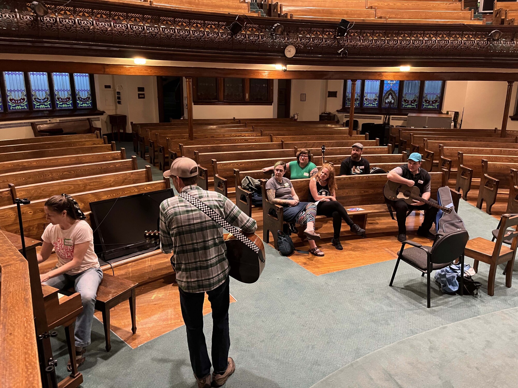 Photograph of a group of musicians sitting, talking and jamming together inside the Emmanuel United Church in Waterloo, Ontario.