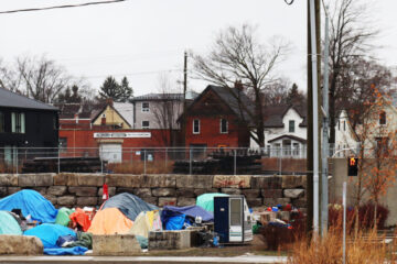 Photograph of the Victoria Street encampment in Kitchener, Ontario. A group of tents sit precariously together behind a traffic sign that reads "No Exit".