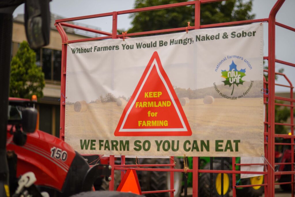 Photo of a sign that reads "Without Farmers You Would Be Hungry, Naked and Sober, KEEP FARMLAND FOR FARMING, WE FARM SO YOU CAN EAT" at the Fight for Farmland rally held in Wilmot Township on August 28th, 2024.