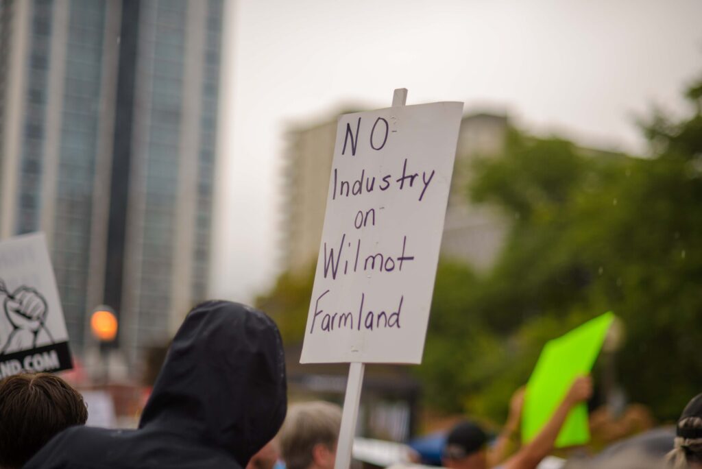 Photo of a sign being held up that reads "NO INDUSTRY ON WILMOT FARMLAND" at the Fight for Farmland rally held in Wilmot Township on August 28th, 2024.