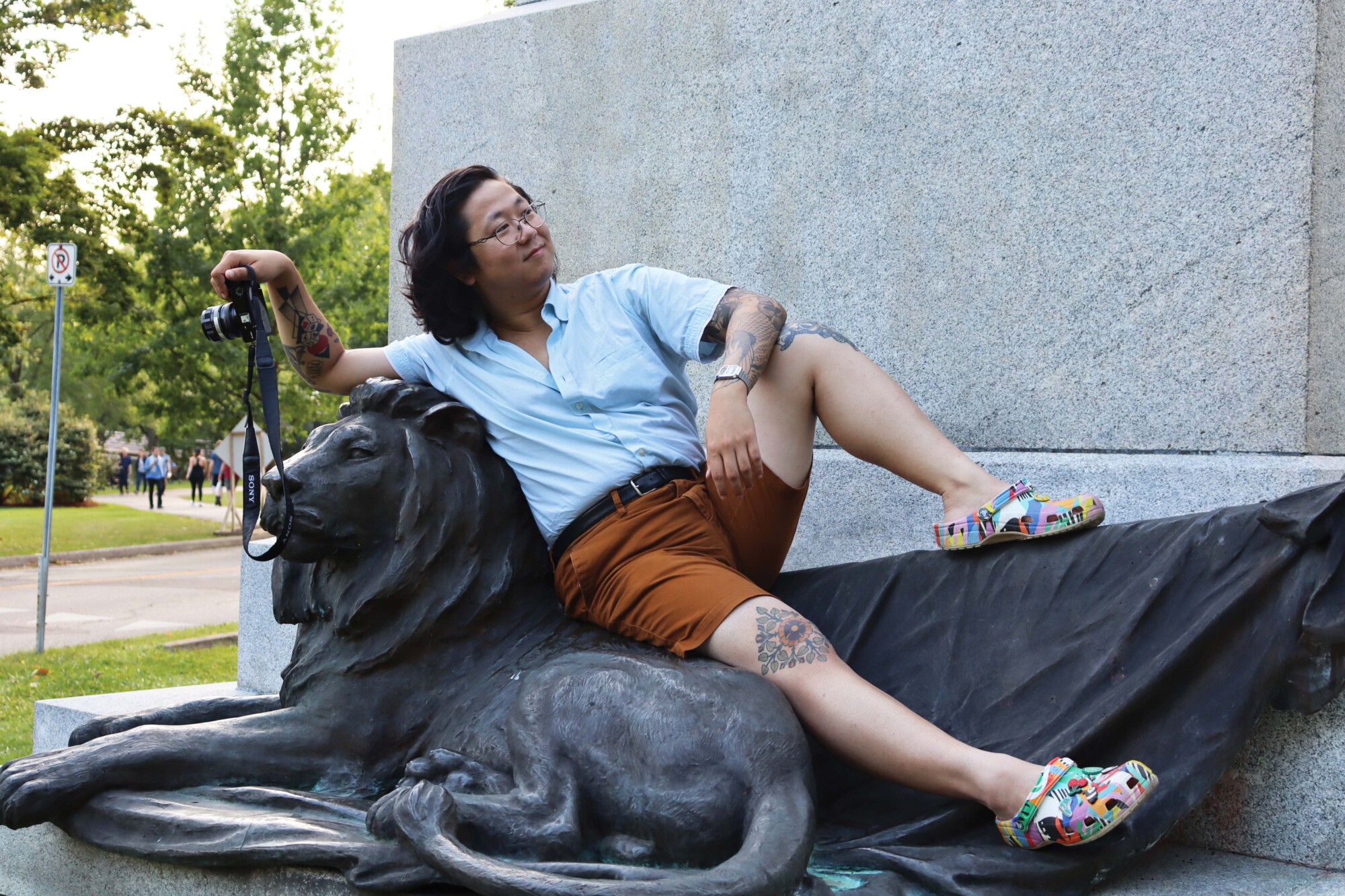 Photo of local photographer Phi Doan lounging on a lion statue while languidly posing with his camera in Willow River Park.