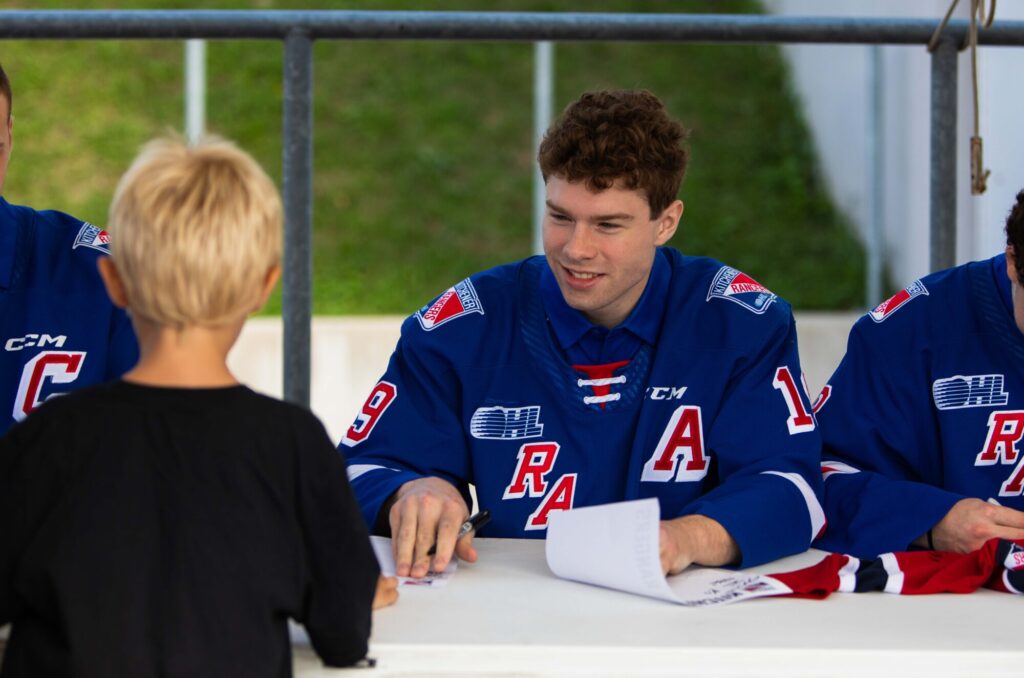 Photo of a hockey player signing an autograph for a child at the Kitchener Ranger's preseason Fan Fest, held at the Kitchener Auditorium on September 1st, 2024.