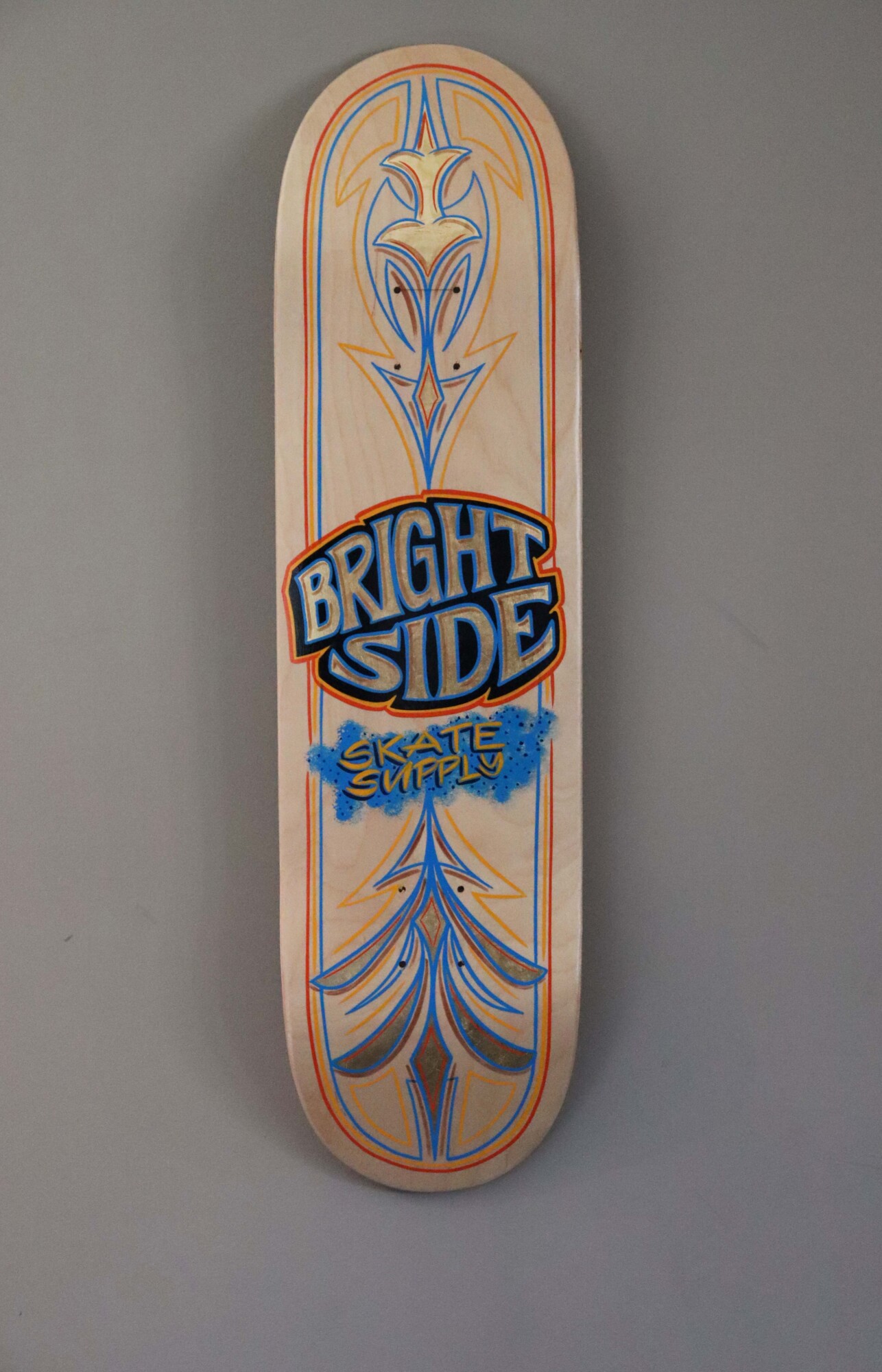 Photo of a skateboard mounted on a wall with the text "Bright Side Skate Supply" printed decoratively on the back of the deck.