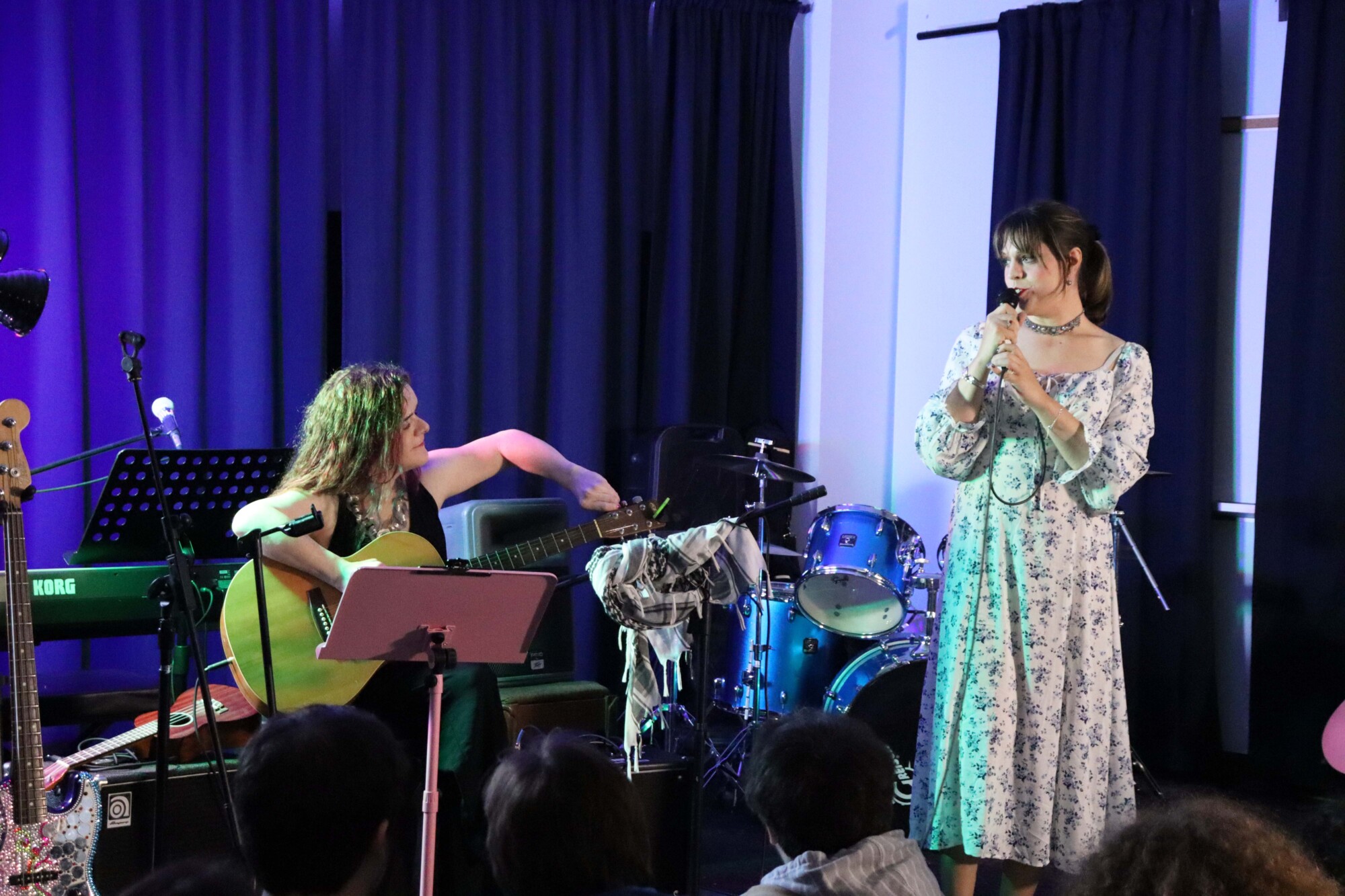 Photo of two performers, one playing acoustic guitar and one singing, onstage during a Harmony Replacement Therapy open-mic night held at 44 Gaukel on September 22nd, 2024.