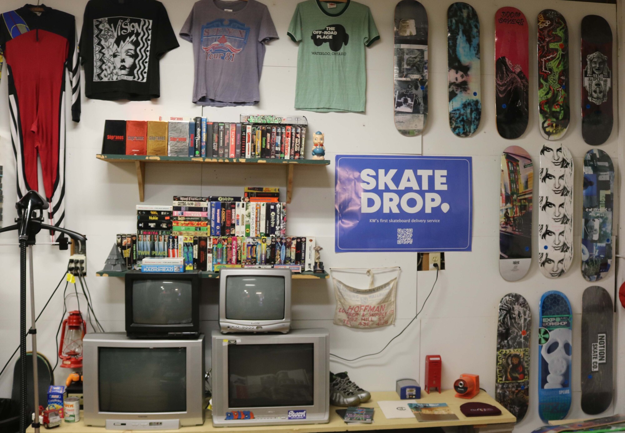 Photo of printed skate decks and a shelf full of DVDs mounted on the wall inside Skate Drop, located at Unit 19, 154 Victoria Street South, Kitchener.