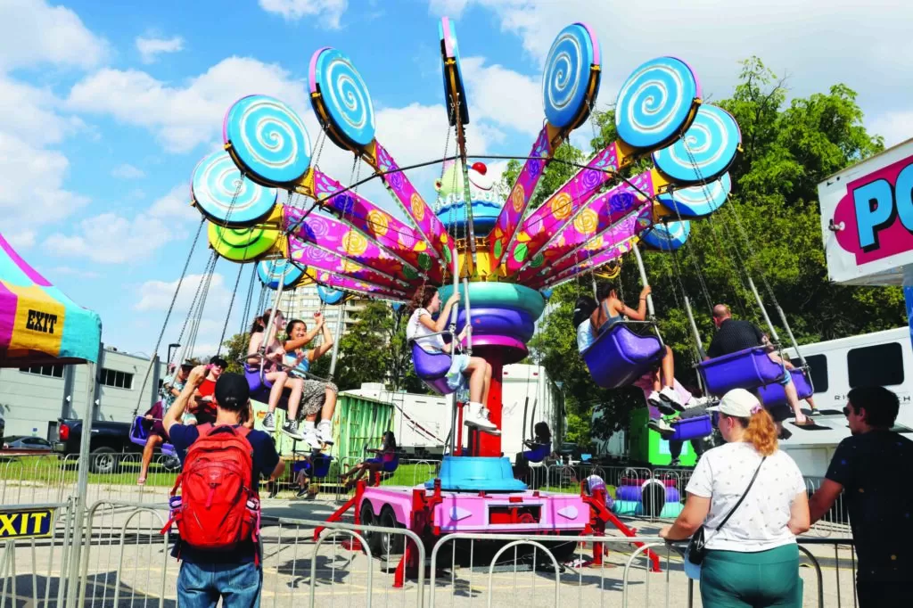 Photo of a bright, candy themed carnival ride being enjoyed by visitors of the 2024 Waterloo Region Busker's Carnival, also called Busker Fest.